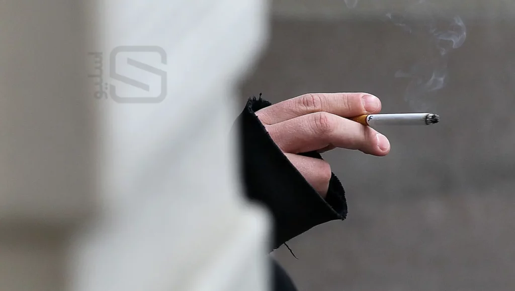 مردی که پشت دیوار در حال سیگار کشیدن است